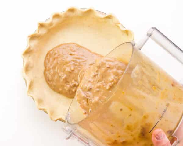 Pecan pie filling is being poured into a prepared pie crust.