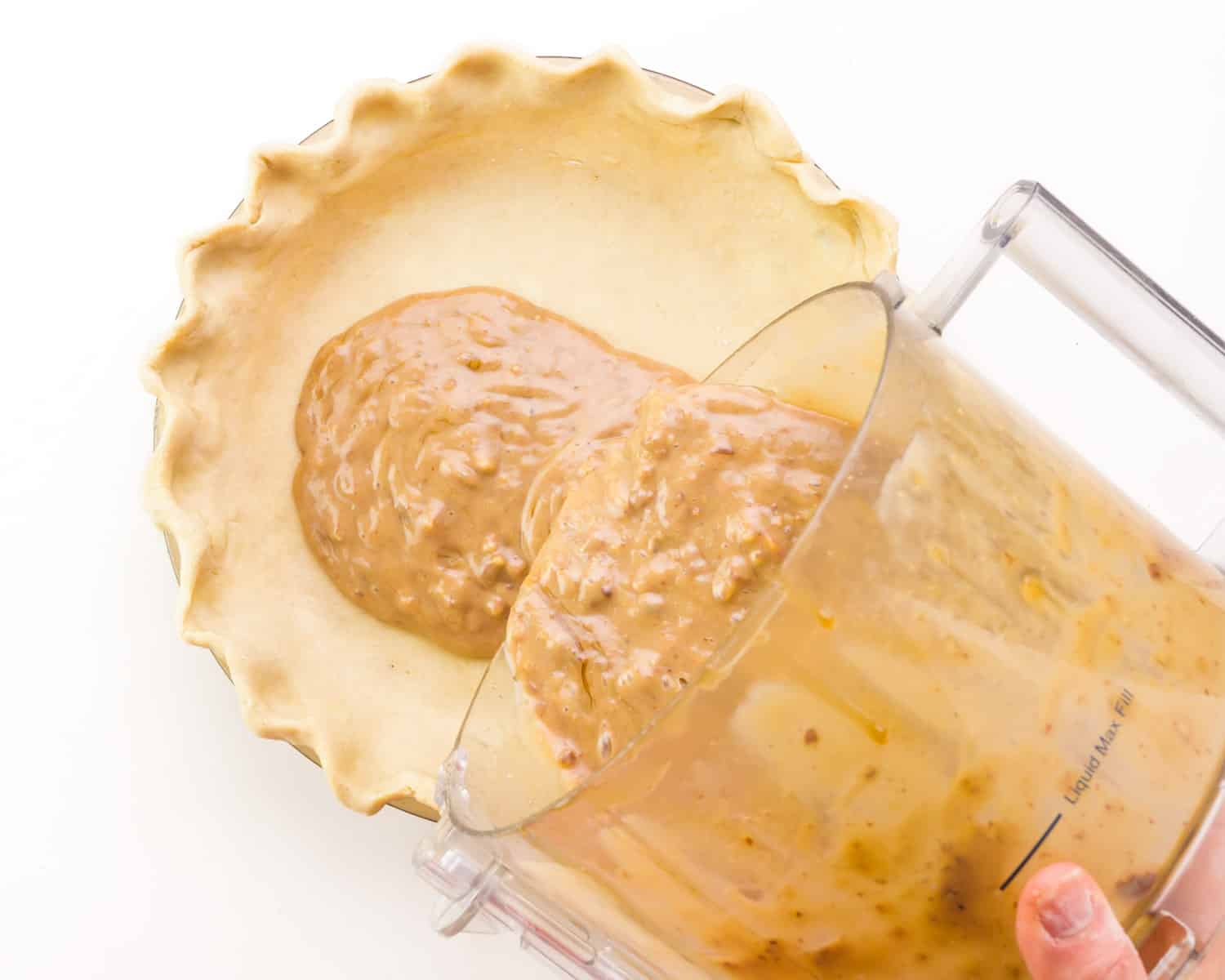 Pecan pie filling is being poured into a prepared pie crust.