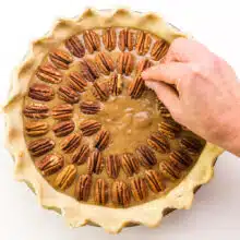 A hand places a pecan on top of a pie, adding them in concentric circles.