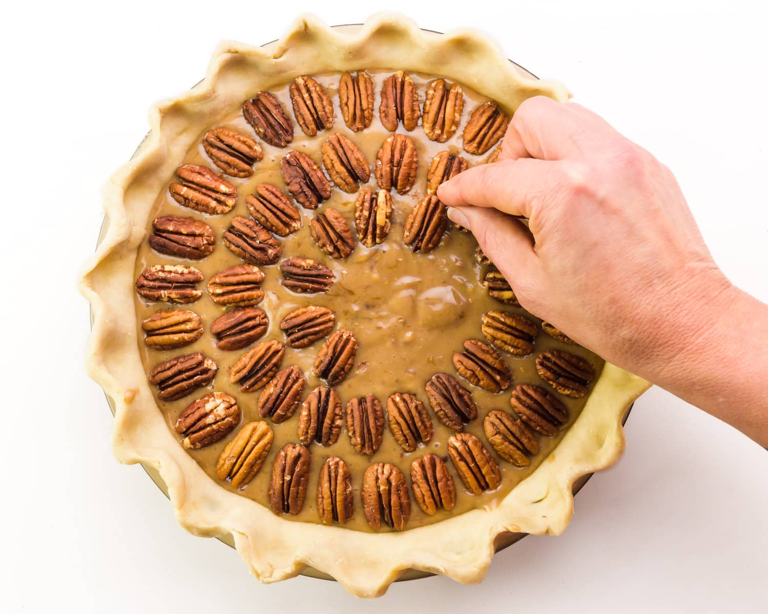 A hand places a pecan on top of a pie, adding them in concentric circles.