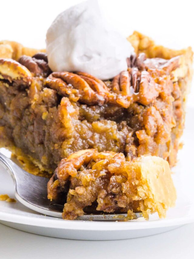 A closeup of a slice of vegan pecan pie on a plate. A bite is sitting on a fork in front of the plate.