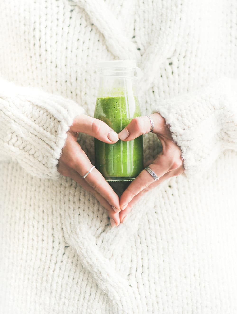 a jar of green smoothie being held by a woman's hands in the shape of a heart