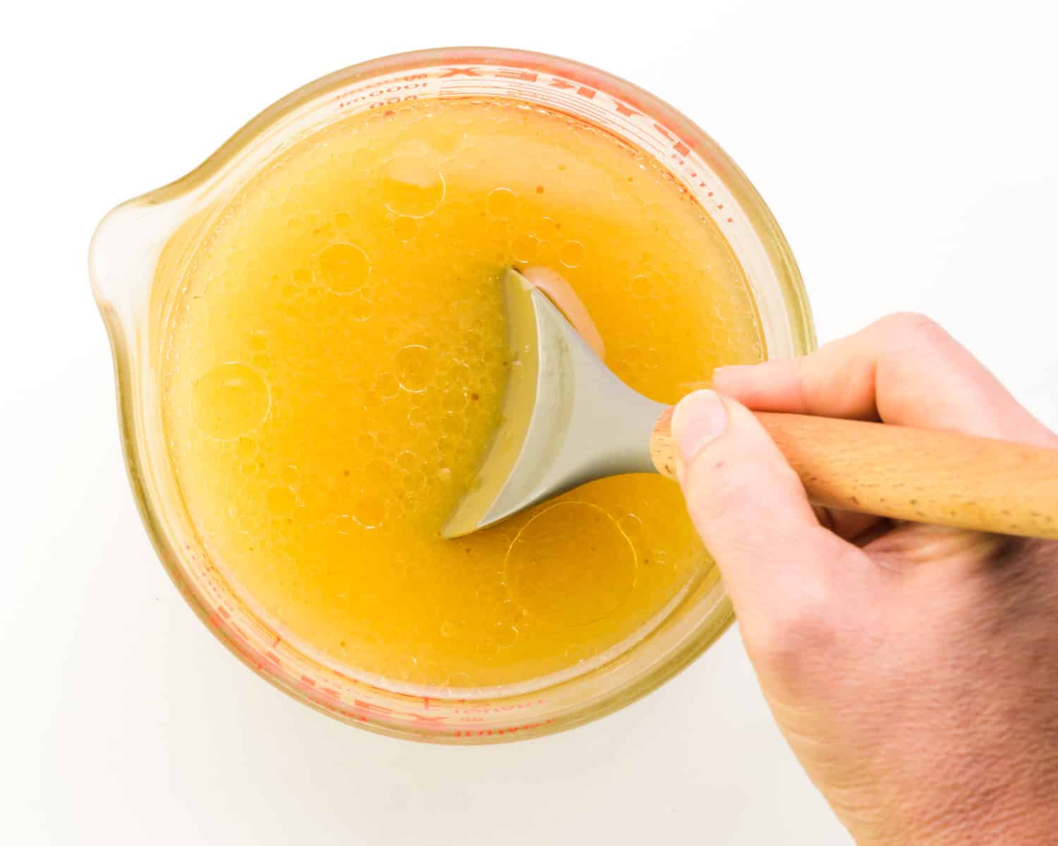A hand holds a spatula, stirring a mixture of water, applesauce and other ingredients.