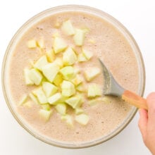 Chopped apples are being stirred into a cake batter.