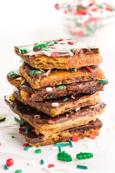 A stack of vegan Christmas crack pieces sits around sprinkles and a bowl of sprinkles in the background.