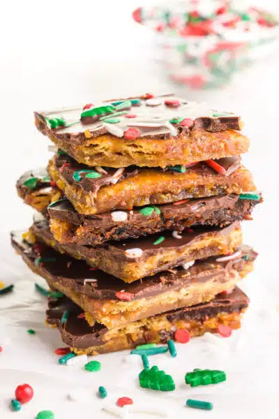 A stack of vegan Christmas crack pieces sits around sprinkles and a bowl of sprinkles in the background.
