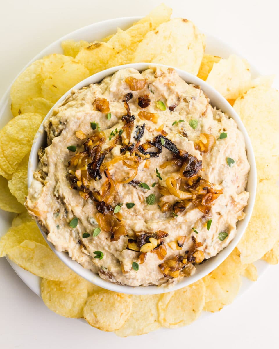 Looking down at a bowl of vegan french onion dip surrounded by potato chips.