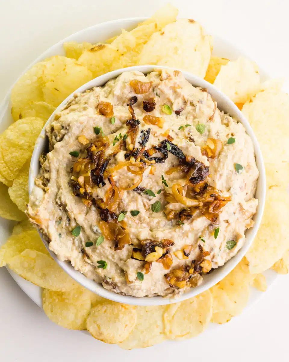 Looking down on a bowl of vegan French onion dip surrounded by potato chips.
