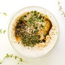 Seasonings and sauce has been added to sour cream in a bowl. Fresh herbs surround the bowl.