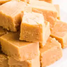 Pieces of vegan peanut butter fudge are stacked on a plate.