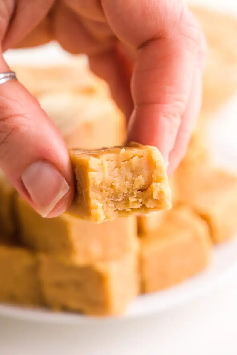 A hand holds a bite of peanut butter fudge with a bite taken out.