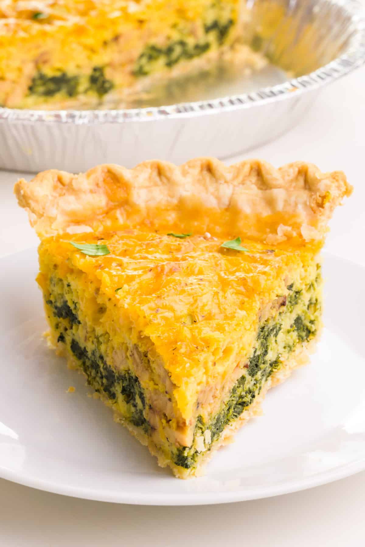 A slice of Just Egg Quiche sits on a plate with more quiche in front of the pan.