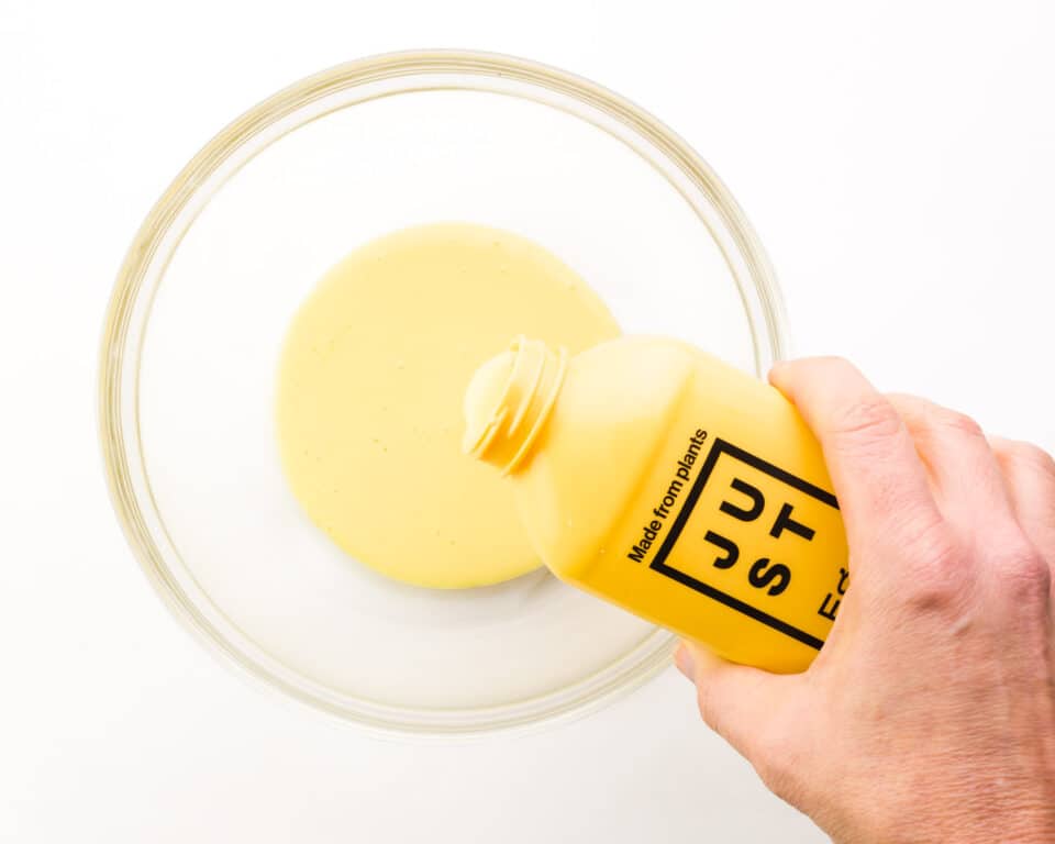 A hand holds a bottle of Just Egg, pouring it into a bowl.