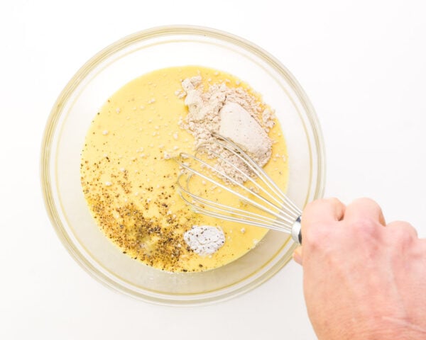 A hand whisks faux egg mixture with several ingredients in a bowl.
