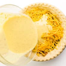 A vegan egg mixture is being poured over a pie crust with cheese and other ingredients.