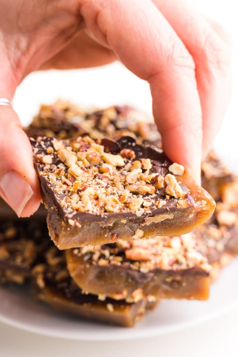 A vegan toffee bar in one hand with more candy on top of a plate.