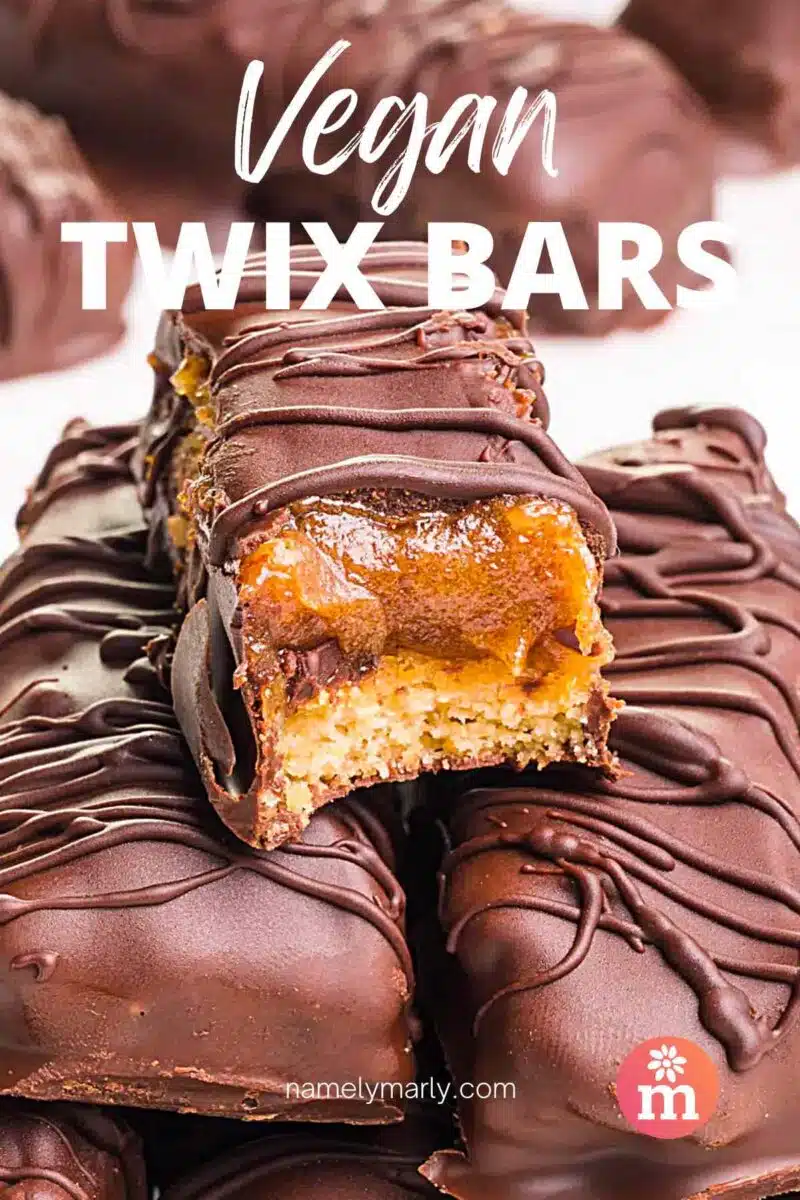 A chocolate cookie bar has a bite taken out, revealing lots of caramel. The text reads, Vegan Twix Bar.