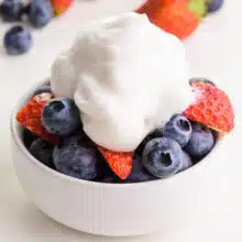 Whipped cream sits on top of a bowl of fresh fruit.