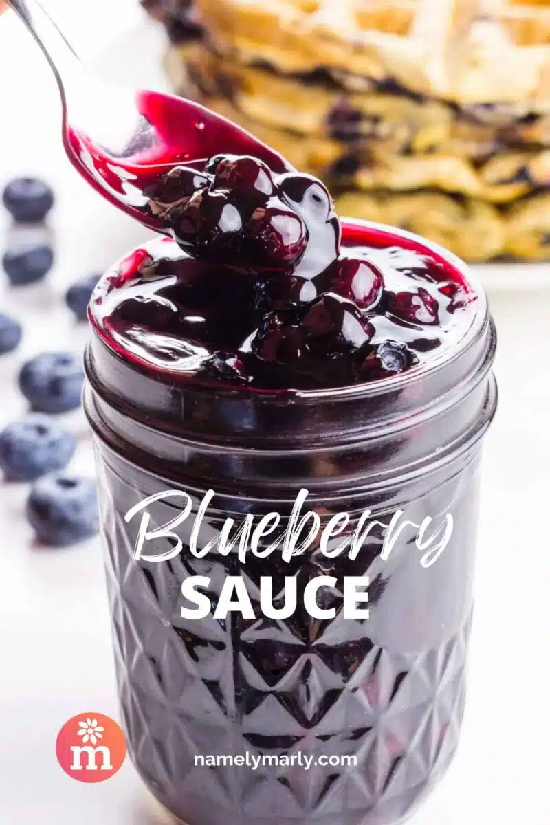 A spoon dishes out blueberry glaze from a mason jar. The text reads, Blueberry Sauce.
