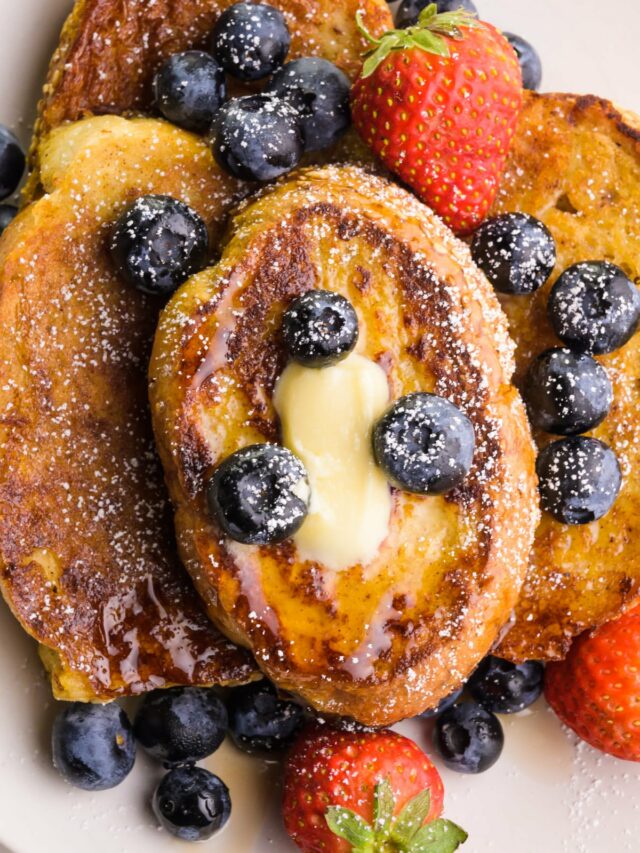 Looking down on slices of French toast on a plate. There are berries and melted butter on top.