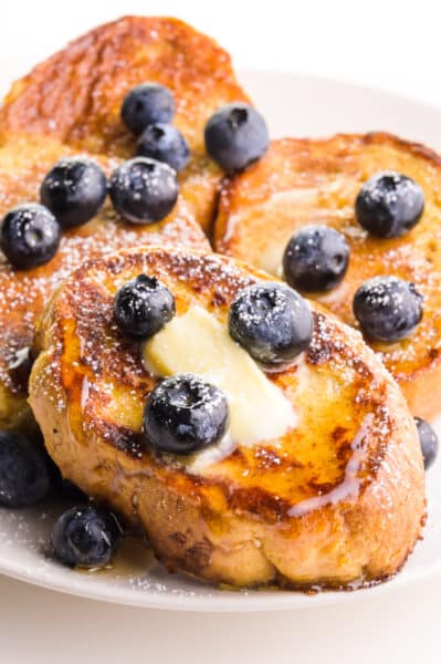 Slices of French toast are topped with blueberries, butter, and maple syrup.