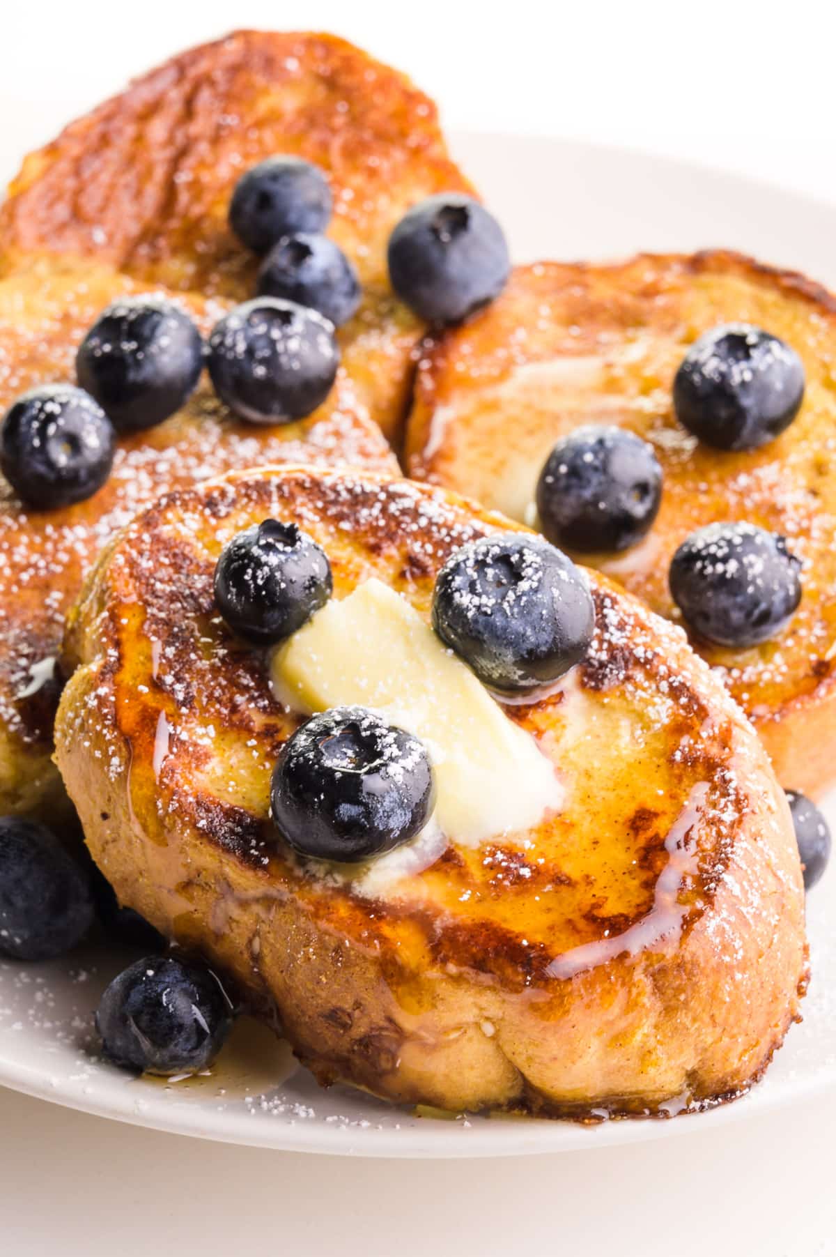 Slices of French toast topped with blueberries, butter and maple syrup.