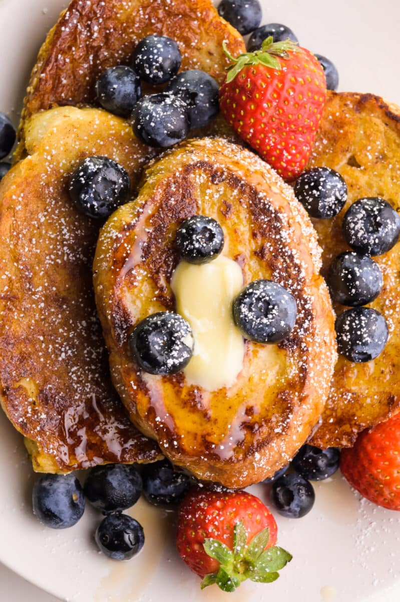 Looking down at pieces of French toast on a plate.  Top with berries and melted butter.