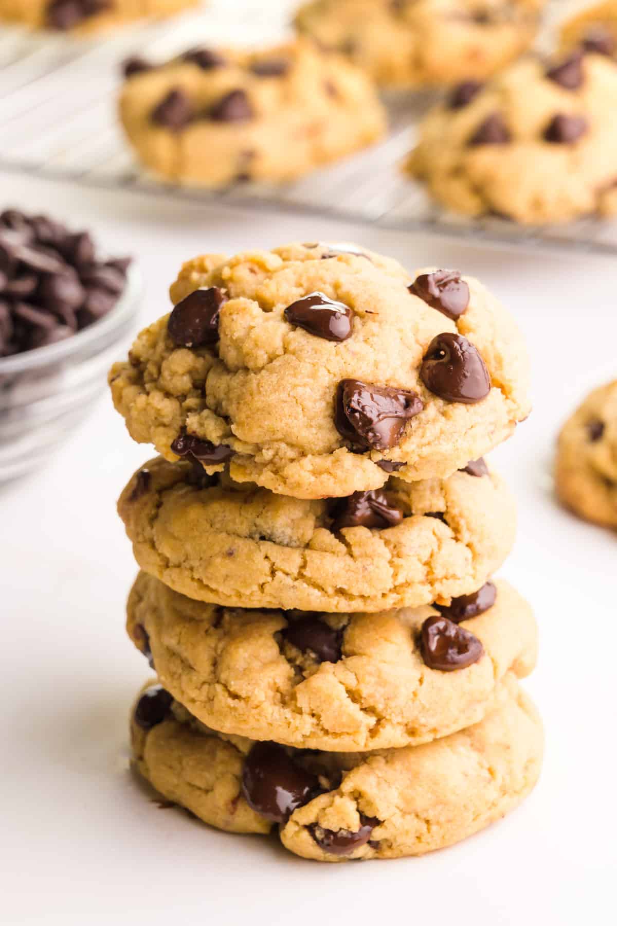 A stack of vegan peanut butter chocolate chip cookies next to a bowl of chocolate chips and more cookies in the background.
