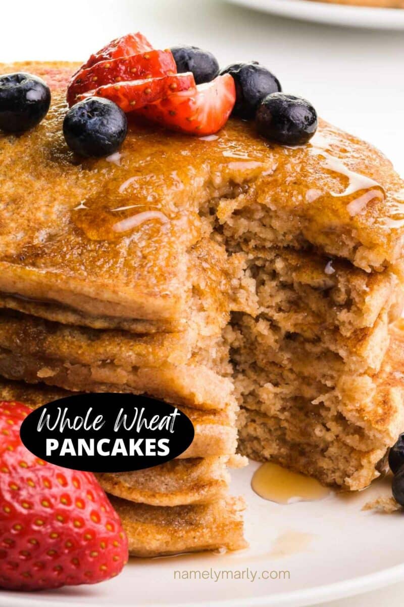 A stack of pancakes has a bite taken out. There are berries on top and beside the pancakes. The text reads, Whole Wheat Pancakes.
