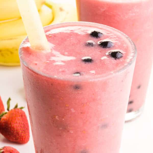 A closeup up of a boba smoothie in a glass sitting next to fresh fruit and another smoothie.