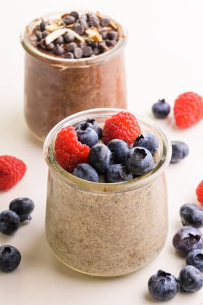 Two dishes of chia pudding sit in front of each other. There are berries on one and chocolate on the other.