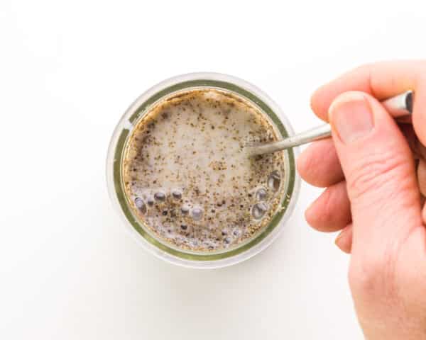 A hand stirs a chia mixture in a small bowl.