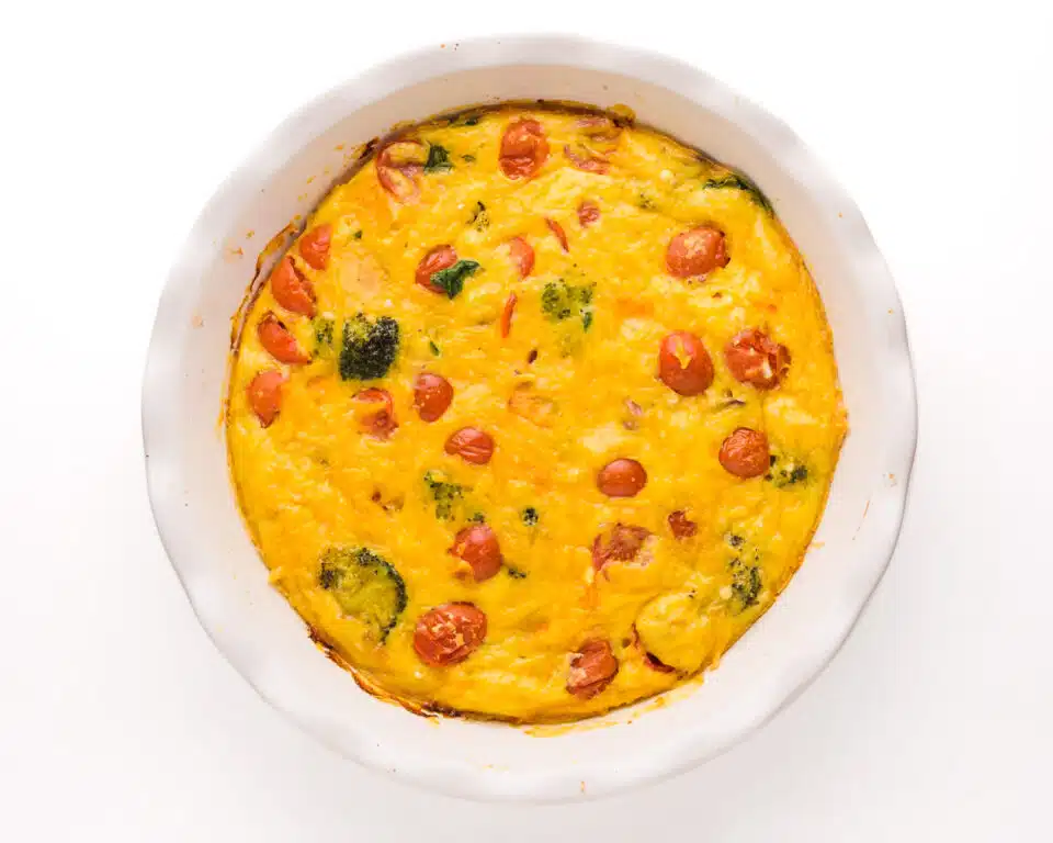 Looking down on a veggie frittata in a white ceramic pie pan.