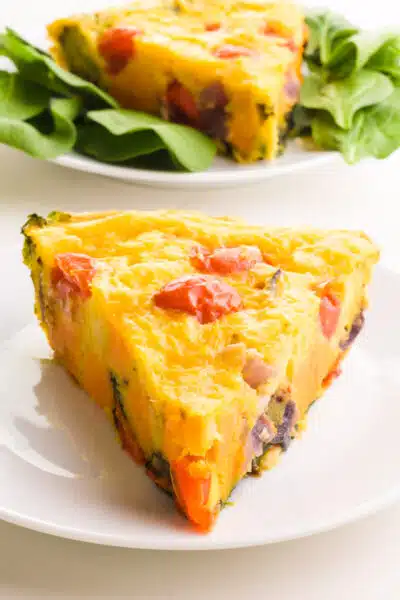 A slice of Just Egg frittata sits on a plate in front of another slice on a plate surrounded by salad greens.