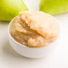 A closeup of pear sauce in a bowl. There are fresh pears in the backgrounds.