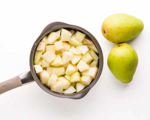 Chopped pears are in a saucepan sitting next to two fresh pears.