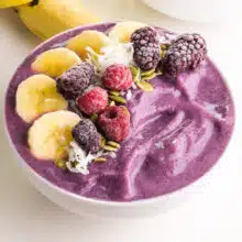 A purple smoothie bowl has frozen fruit on top.