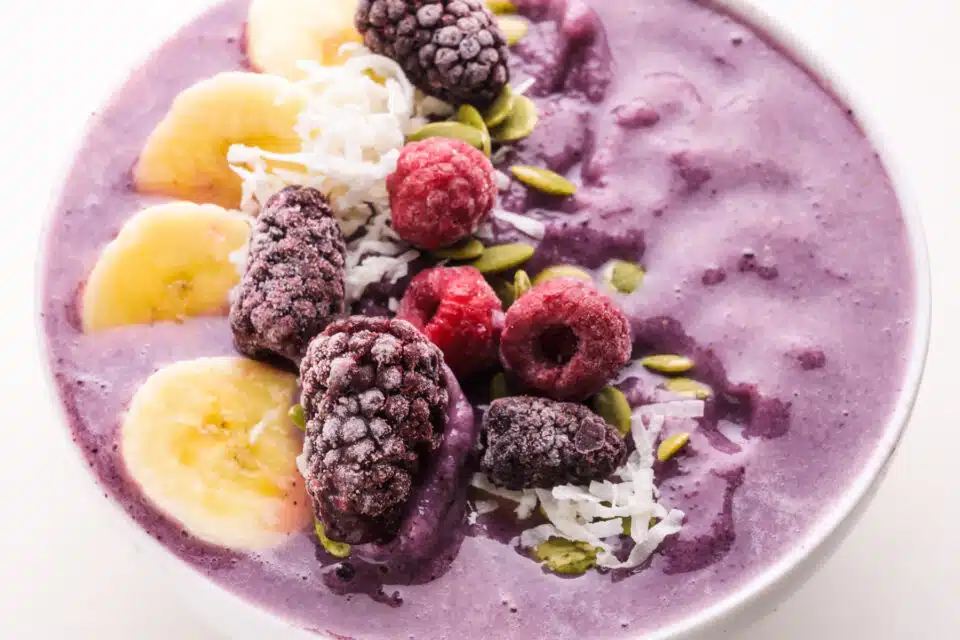 A closeup of a smoothie bowl with purple base topped with frozen and fresh fruits.