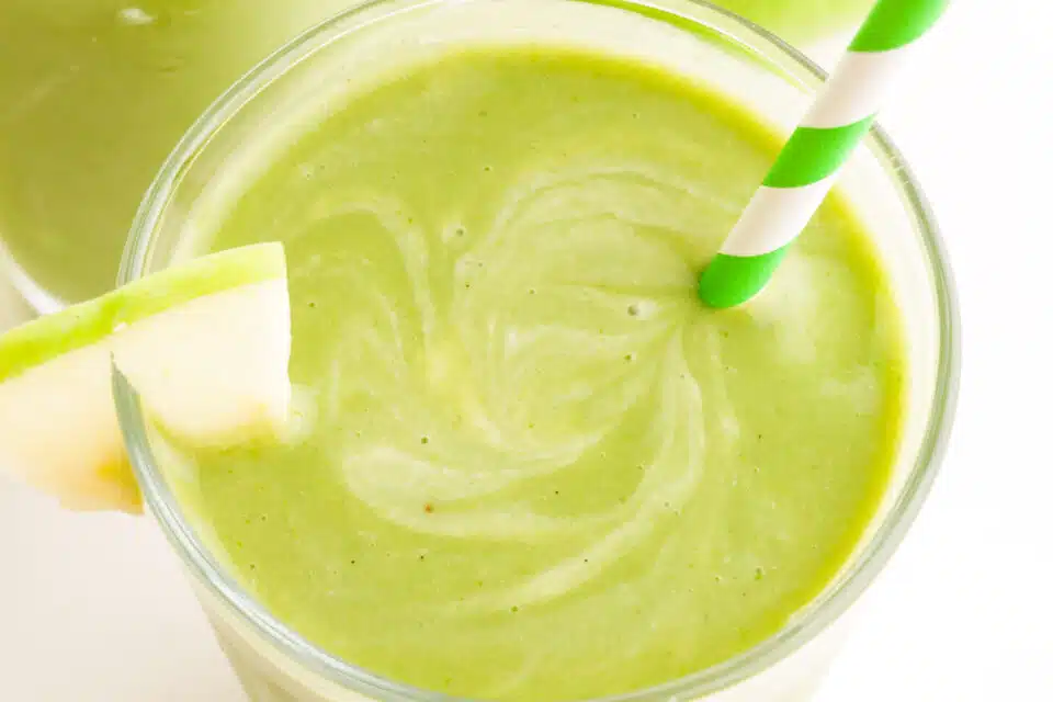 Looking down on a green smoothie with a straw and an apple slice.