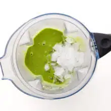 Ice is in a blender jar along with a green smoothie mixture.