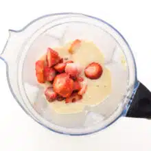 Strawberries are in a blender with other smoothie ingredients.