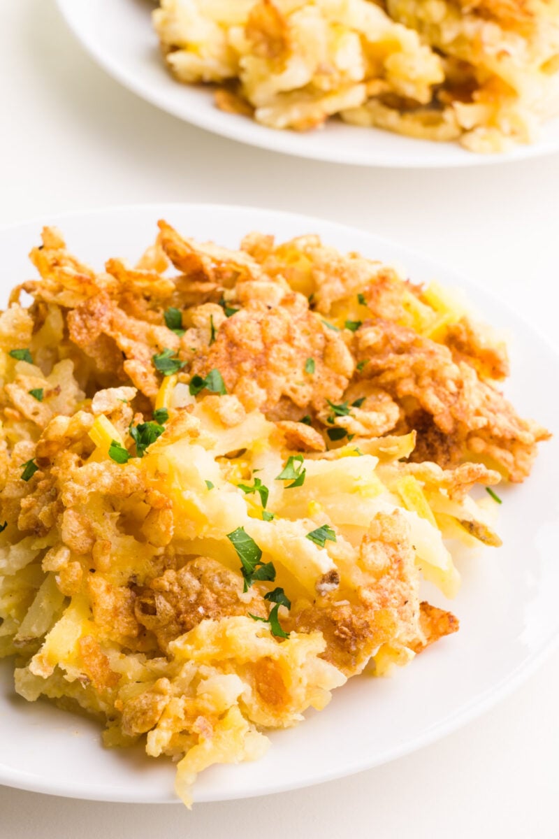 A serving of vegan cheesy potatoes sits on a plate in front of another plate.