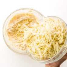 Thawed frozen hash brown potatoes are being poured into a bowl with a creamy mixture.