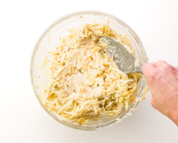 A hand holds a spatula, stirring potatoes with a creamy mixture.