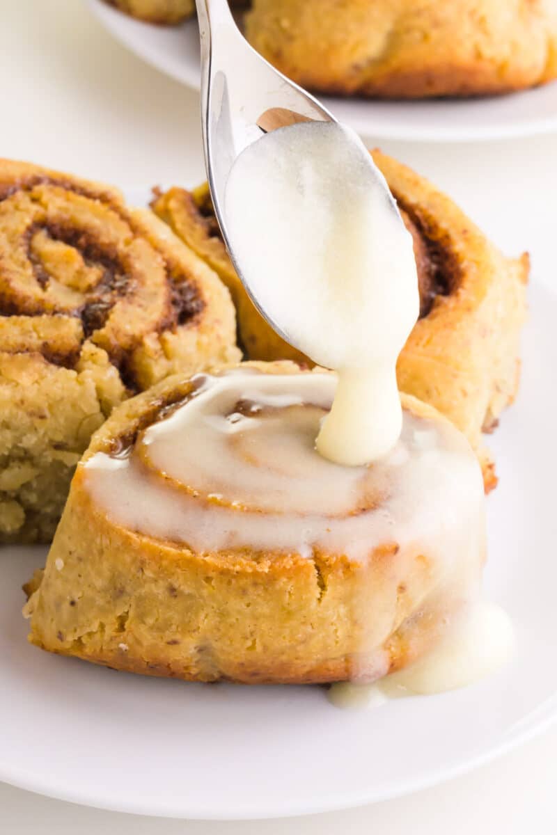 A spoonful of icing drizzles over a vegan gluten-free cinnamon roll.