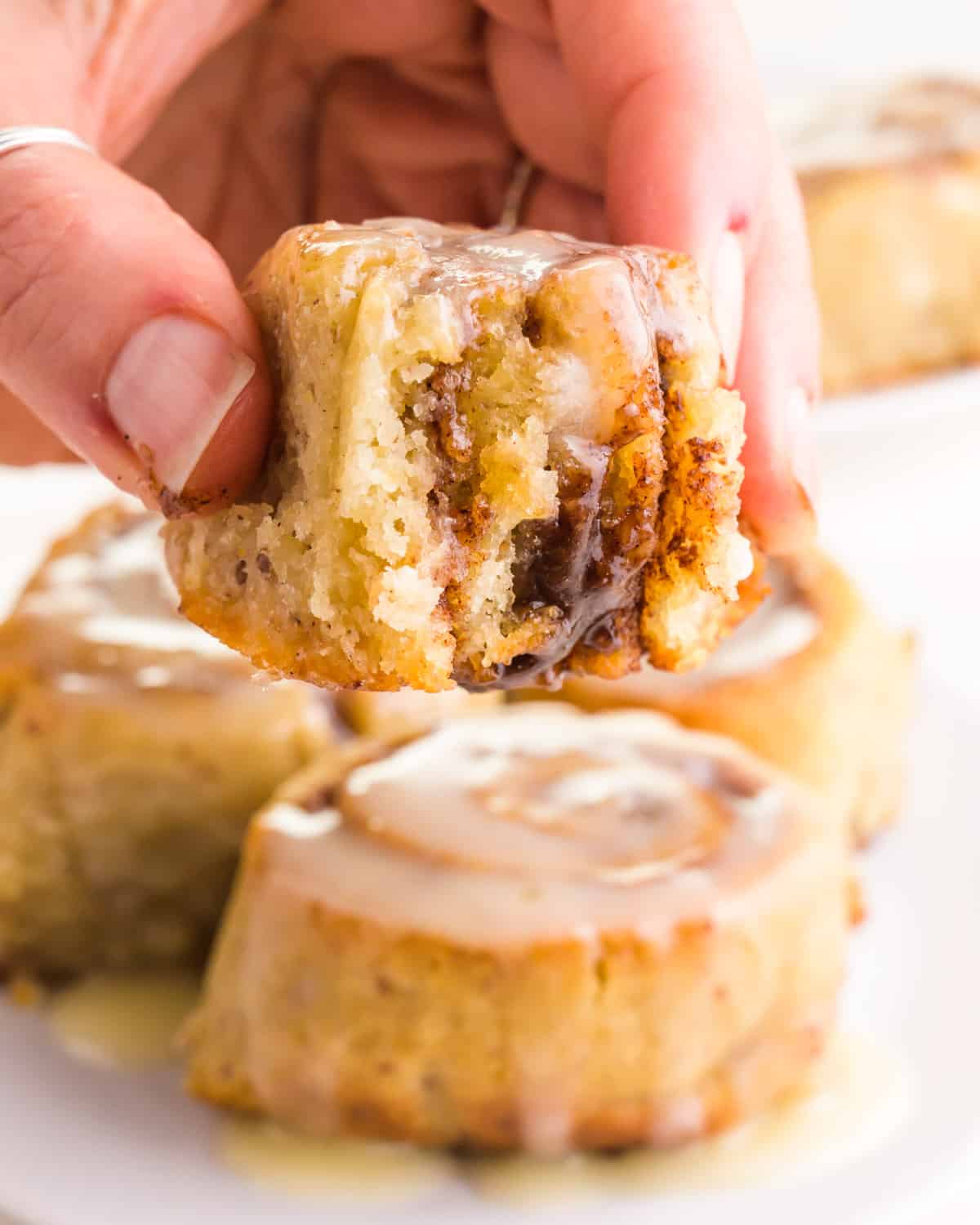 A hand holding a cinnamon roll with a bite, hovering over more cinnamon rolls.