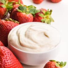 A bowl of vegan mascarpone sits around fresh strawberries.