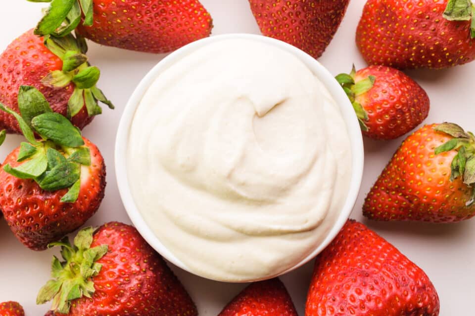 Looking down on a bowl of dairy-free mascarpone sitting around fresh strawberries.