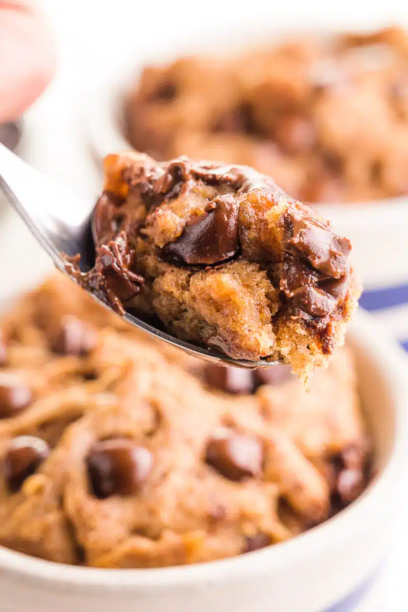 A spoonful of cookie hovers over a dish with more mug cookie in it.