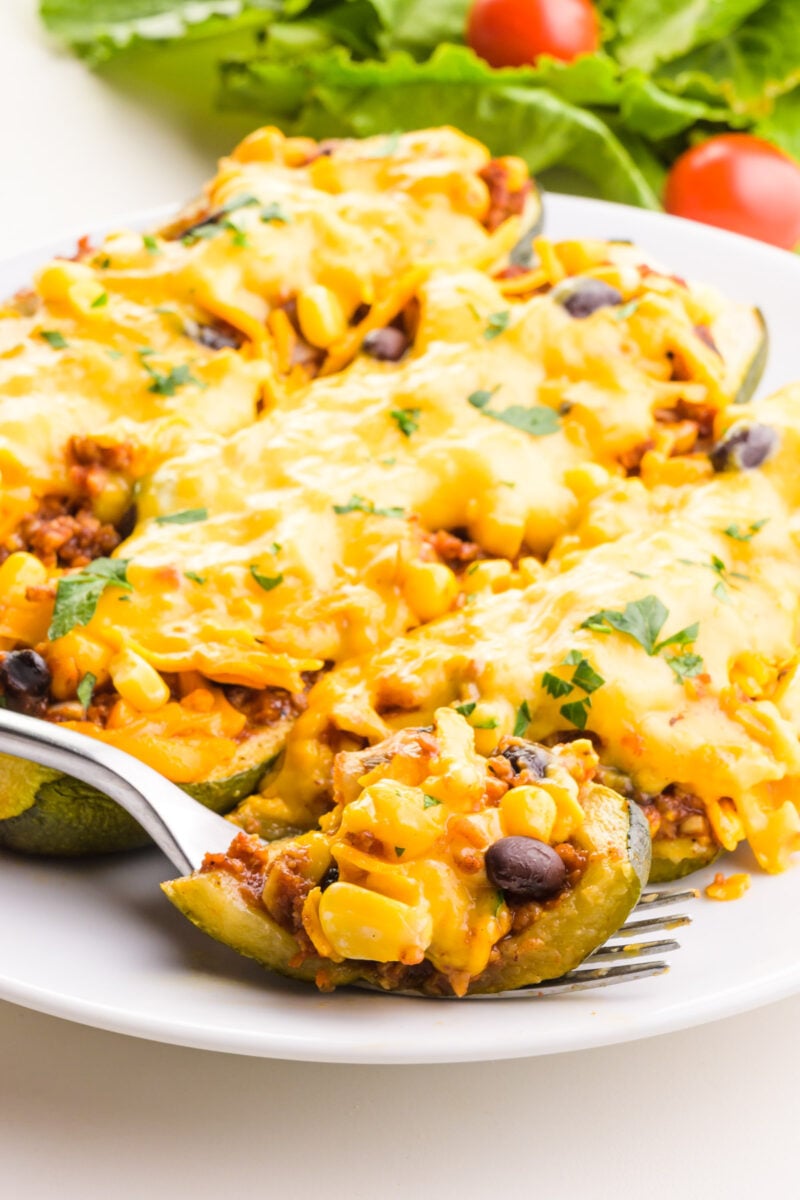 Cheese-topped zucchini boats are on a plate sitting in front of a salad.